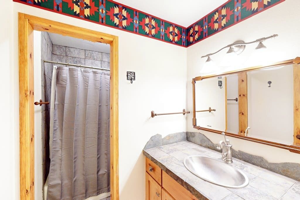 A bathroom with a shower curtain, a sink, a mirror, and a decorative border.