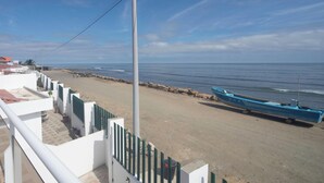 A beach view with a boat, a clear sky, and a white building with a green fence. - Perfect 3-bedroom Modern and Spacious Beach House (Manabí)