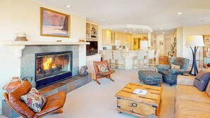 A living room with a fireplace, leather sofas, a coffee table, and a kitchen in the background.
