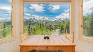 A wooden table with binoculars, a window with a mountain view, and a chair.
