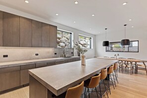 Eine moderne Küche mit einer großen Kochinsel, Holzschränken und einem Essbereich mit einem langen Tisch und Stühlen.