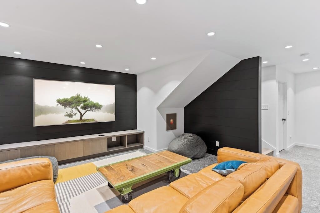 Una sala de estar moderna con un televisor de pantalla plana grande, sofás de cuero, una mesa de centro y un diseño de techo único.