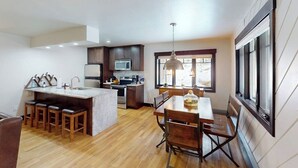 Una cocina moderna con una isla central, taburetes de bar, una mesa de comedor con sillas y un ventanal grande.