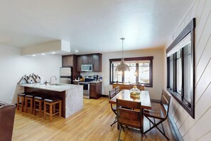 A modern kitchen with a central island, bar stools, a dining table with chairs, and a large window. - Cozy ski retreat with pool, hot tub, sauna, balcony & mountain views (Steamboat Springs)