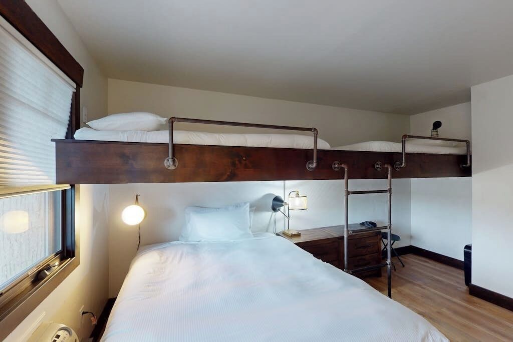 Una camera con letto a castello, una scrivania e una lampada, una finestra con tende e un riscaldatore a parete.