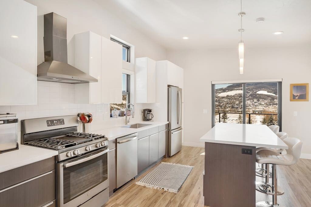A modern kitchen with stainless steel appliances, white cabinetry, and a large window offering a scenic view.