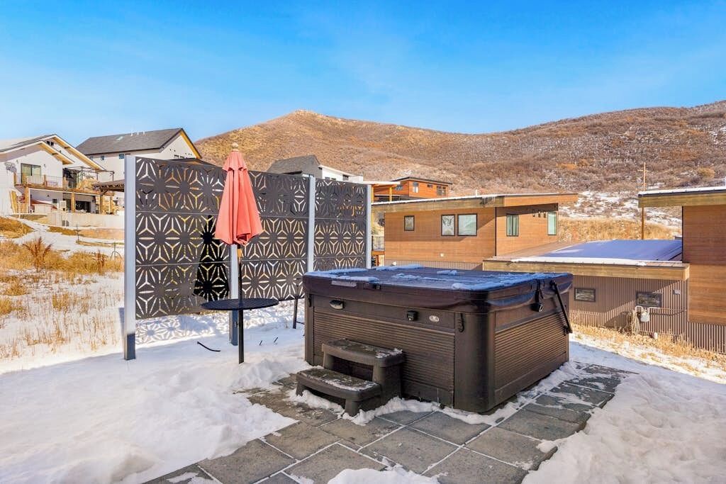 A hot tub in a snowy outdoor area with a patterned fence and a red umbrella.