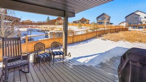 Ett takförsett utomhusområde med trädeck, en grill och utsikt över bostadshus.