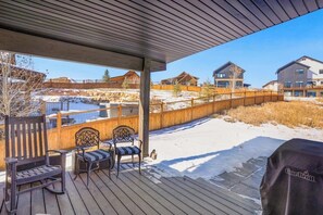 Ein überdachter Außenbereich mit Holzdeck-Sitzgelegenheiten, einem Grill und Blick auf Wohnhäuser.