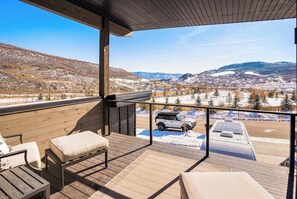 Eine Holzterrasse mit Sitzgelegenheiten im Freien, Blick auf eine verschneite Landschaft und ein geparktes Fahrzeug.