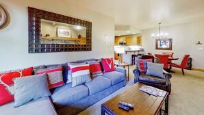 A living room with a sofa, coffee table, and a dining area with a red chair and table. - EagleRidge Lodge 210 Mountain view condo with pool, hot tubs & gym - short walk to gondola (Steamboat Springs)