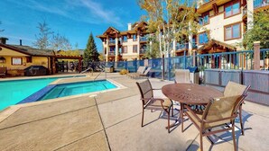 A pool area with a table and chairs, a covered seating area, and a building with balconies. - EagleRidge Lodge 210 Mountain view condo with pool, hot tubs & gym - short walk to gondola (Steamboat Springs)