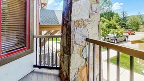 A balcony with a stone pillar, a wooden railing, and a window with blinds. - EagleRidge Lodge 210 Mountain view condo with pool, hot tubs & gym - short walk to gondola (Steamboat Springs)
