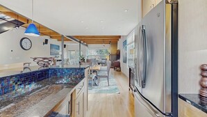 Una cocina moderna con un refrigerador grande, vigas de madera en el techo y una lámpara colgante azul.