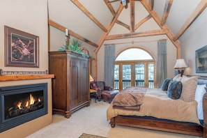 A bedroom with a fireplace, wooden beams, a bed, a desk, and a window. - Two-story, dog-friendly home with fireplace & W/D (Mountain Village)