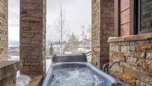 Een jacuzzi in een buitengebied met stenen muren en uitzicht op met sneeuw bedekte bergen.