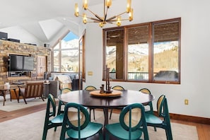 Ein Essbereich mit rundem Tisch, Stühlen, einer Chandelüster, einem Kamin aus Stein und einem Fernseher.