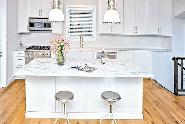 A kitchen with white cabinetry, a marble island, two bar stools, a gas stove, a microwave, and pendant lighting. - Dog-friendly home close to Telluride with W/D, balcony & yard (Mountain Village)