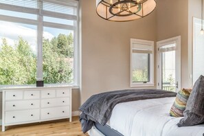 A bedroom with a large window, a bed with a gray blanket, a white dresser, and a hanging light fixture. - Dog-friendly home close to Telluride with W/D, balcony & yard (Mountain Village)
