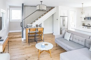 A modern kitchen with a built-in stove, a dining area with a wooden table and chairs, a gray sofa, and a staircase with a metal railing. - Dog-friendly home close to Telluride with W/D, balcony & yard (Mountain Village)
