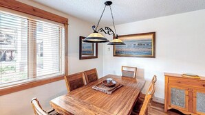 A dining area with a wooden table, chairs, a chandelier, and a window with blinds. - TL1112 | Mountain Condo | Pool | Hot Tubs | Winter Shuttles (Steamboat Springs)