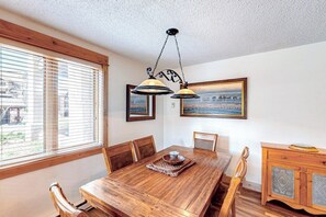 Ein Essbereich mit Holztisch, Stühlen, einer Chandelierleuchtre und einem Fenster mit Jalousien.