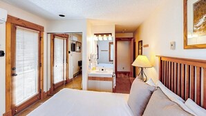 A hotel room with a bed, a bathroom with a sink and mirror, and a hallway leading to another room. - TL1112 | Mountain Condo | Pool | Hot Tubs | Winter Shuttles (Steamboat Springs)