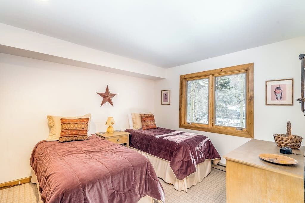 Un dormitorio con dos camas, decoración de estrellas, una ventana con vistas y un escritorio con una cesta.