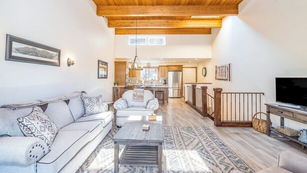 A spacious living room with a wooden ceiling, a sofa, a coffee table, and a TV. - River-view condo with fireplace & hot tub - walk to gondola & Main St (Telluride)