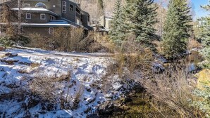 A two-story house with a sloped roof, surrounded by trees and a stream. - River-view condo with fireplace & hot tub - walk to gondola & Main St (Telluride)