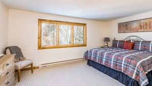 A bedroom with a large window, a bed with a plaid bedspread, a bedside table with a lamp, and a dresser. - River-view condo with fireplace & hot tub - walk to gondola & Main St (Telluride)