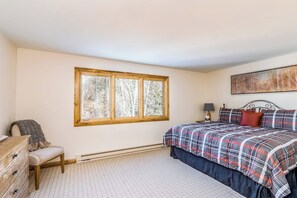 Ein Schlafzimmer mit einem großen Fenster, einem Bett mit kariertem Überwurf, einem Nachttisch mit Lampe und einer Kommode.