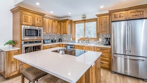 A modern kitchen with wooden cabinets, stainless steel appliances, and a large island. - River-view condo with fireplace & hot tub - walk to gondola & Main St (Telluride)