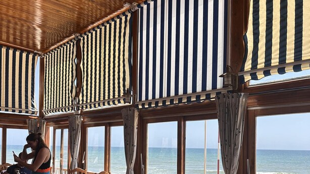 Een restaurant met tafels, stoelen, grote ramen en uitzicht op zee.