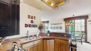 Una cuina moderna amb un cartell de 'EAT & DRINK', armaris de fusta, un rentaplats i una finestra gran amb vistes a una terrassa.