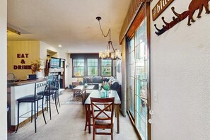 A modern kitchen with a bar area, a dining table with chairs, a sofa, and a large window with a view. - Amazing home close to Granby Ranch with shared hot tub, pool, & WiFi (Granby)