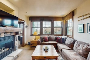 A living room with a fireplace, a sofa, a coffee table, and large windows. - Amazing home close to Granby Ranch with shared hot tub, pool, & WiFi (Granby)
