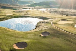 Ein Golfplatz mit Teich, Sandbunkern und einem geschwungenen Weg.