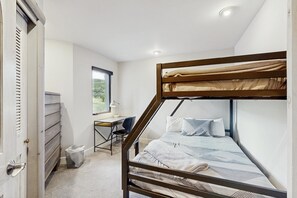 Ein Schlafraum mit Etagenbetten, einem Schreibtisch und Stuhl, einem Fenster mit Blick und einer Tür.