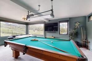 Ein Billardtisch mit Blick auf eine gebirgige Landschaft durch große Fenster.