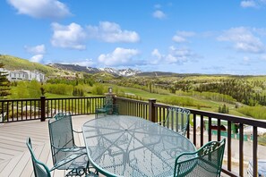 Eine Terrasse mit rundem Tisch und Stühlen, mit Blick auf eine gebirgige Landschaft und Gebäude in der Ferne.