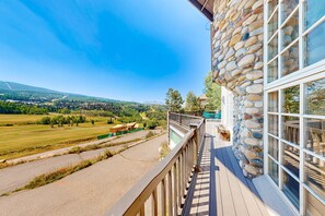 Ein Balkon mit Steinmauer, Blick auf eine grüne Landschaft und einem strahlend blauen Himmel.