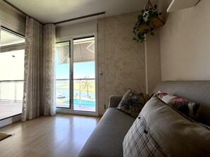 Una sala de estar con sofá, puerta corrediza de vidrio que da a un balcón y una planta colgante.