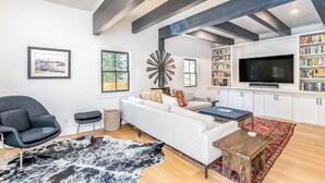 Una sala de estar moderna con un sofá blanco, un sillón negro y un televisor. Hay estanterías y un ventanal grande.