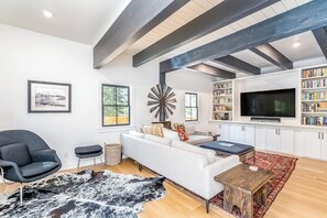 Ein modernes Wohnzimmer mit einem weißen Sofa, einem schwarzen Sessel und einem Fernseher. Es gibt Bücherregale und ein großes Fenster.