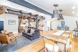 Ein modernes Wohnzimmer mit einer Couch, Sesseln, einem Esstisch und einer Treppe, die zur Küche führt.