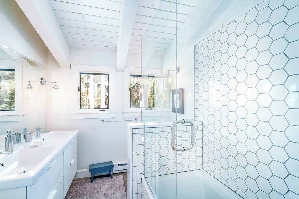 Ein modernes Badezimmer mit einem großen Spiegel, einer Duschkabine aus Glas und einer Wand mit weißen, sechseckigen Fliesen.