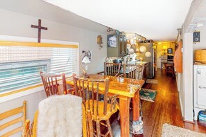 A dining area with a wooden table and chairs, a cross on the wall, and a window with blinds.