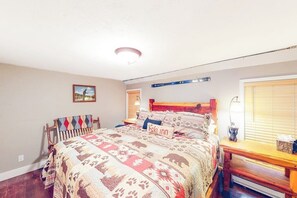 A bedroom with a bed, a headboard, a nightstand, a window with blinds, and a wall-mounted shelf.