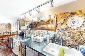A kitchen with a stone wall, a clock, and various kitchen items.